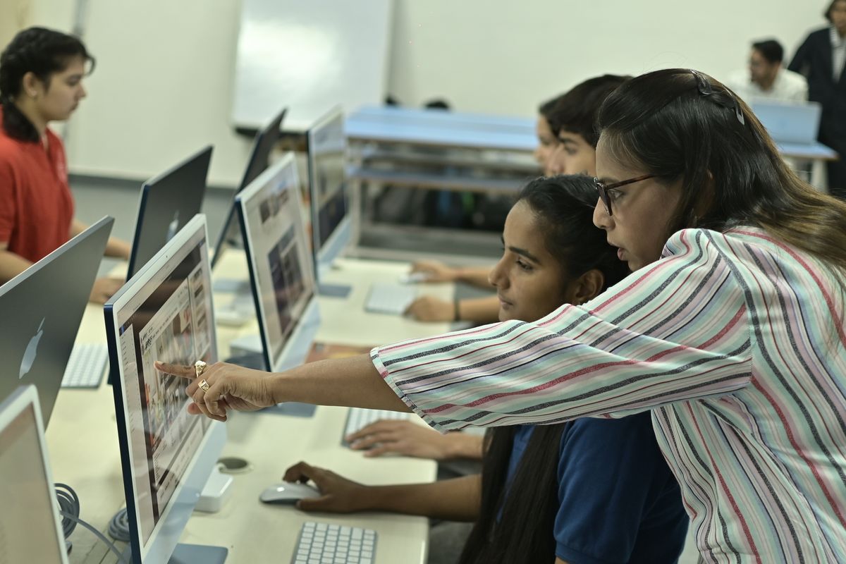 An instructor points at a screen, helping a student review their work in a computer lab.