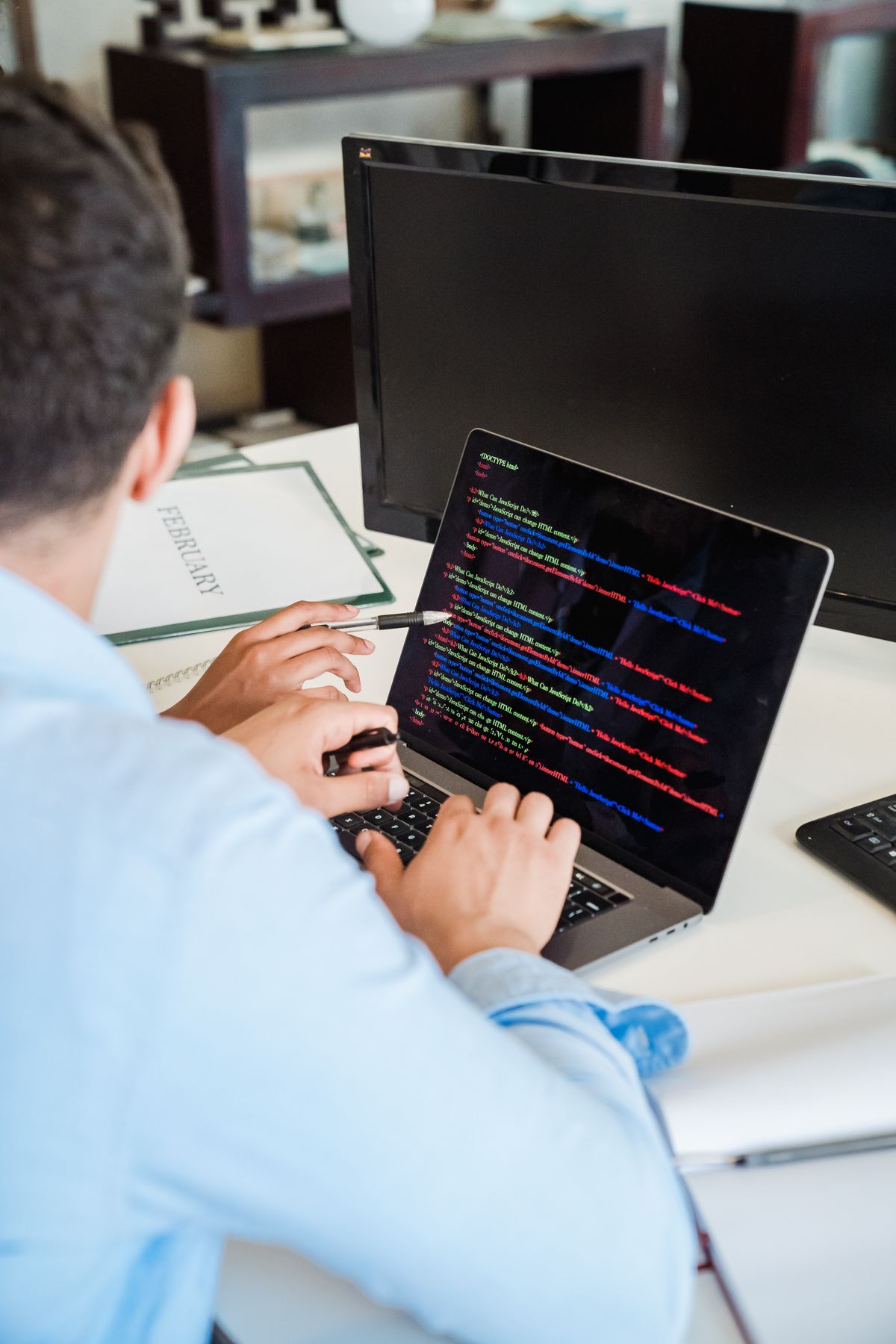 Someone writing HTML and JavaScript code on a laptop in a bright workspace.